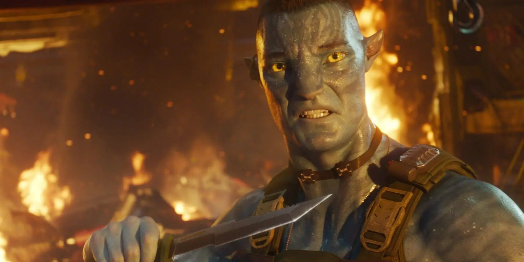 fq64vy quaritch in his na vi form holding a knife while a fire rages behind him in avatar the way of water